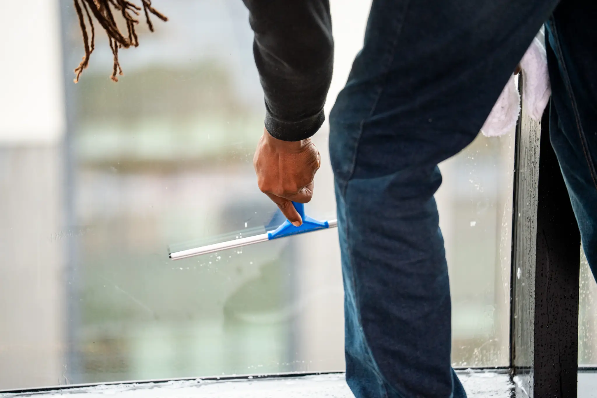 premier janitorial employee cleaning a window with a squeegee