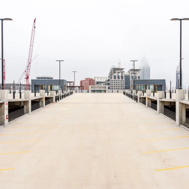 Empty parking deck with blue accessible-space markings, construction cranes, and a modern city skyline beneath an overcast sky.