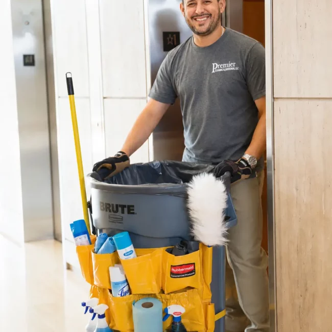 premier cleaning janitor walking with a janitorial trash can lined with janitorial cleaning supplies