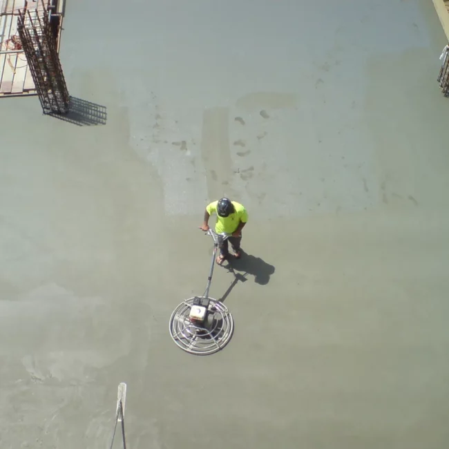 Worker running a rotary floor machine across a concrete floor